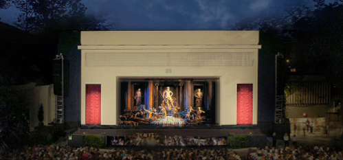 A large outdoor theater stage with a dramatic backdrop and a seated audience, illuminated at night.