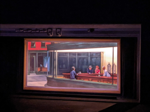 A painting of a diner scene with people sitting at a counter, framed in a theater setting.