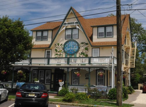 A charming, multi-story inn with a decorative sign, surrounded by greenery and parked cars.