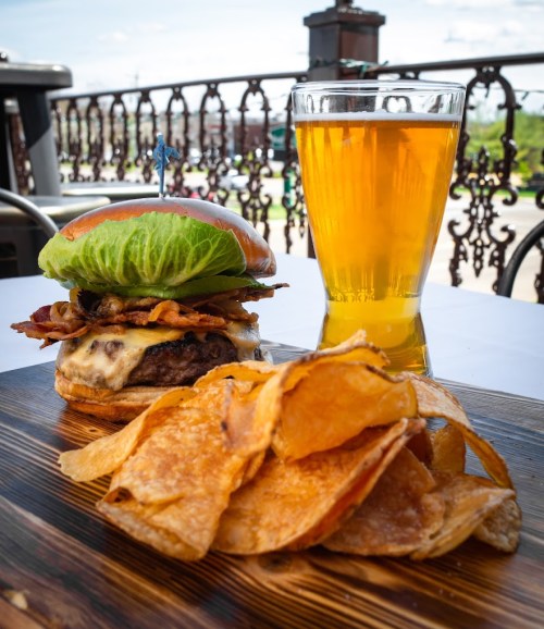 A juicy burger with bacon and lettuce, served with crispy chips and a glass of golden beer on a wooden platter.