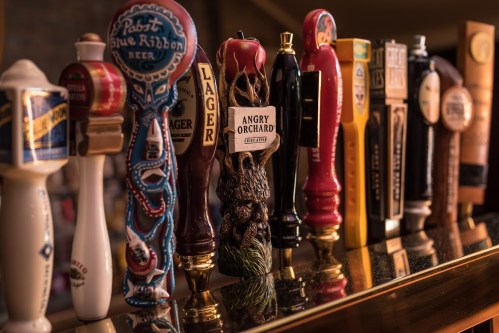 A row of colorful beer taps featuring various brands and styles, displayed on a bar counter.