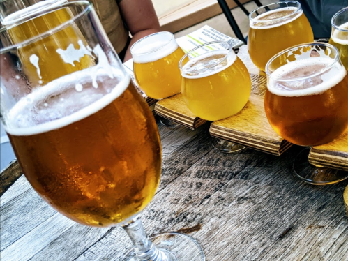 A close-up of a glass of beer with a flight of various beers in small glasses on a wooden table.