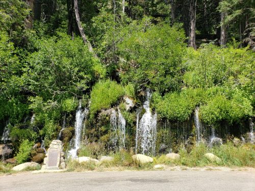 A serene waterfall cascading over rocks, surrounded by lush greenery and trees in a natural setting.