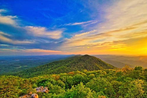 A vibrant sunset over rolling green hills and valleys, with a colorful sky filled with clouds.