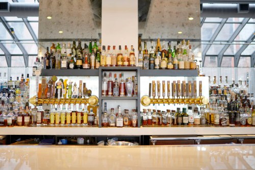 A well-stocked bar featuring shelves of various liquor bottles and a row of beer taps against a modern backdrop.