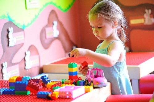 A young girl builds with colorful blocks at a play table in a bright, cheerful environment.