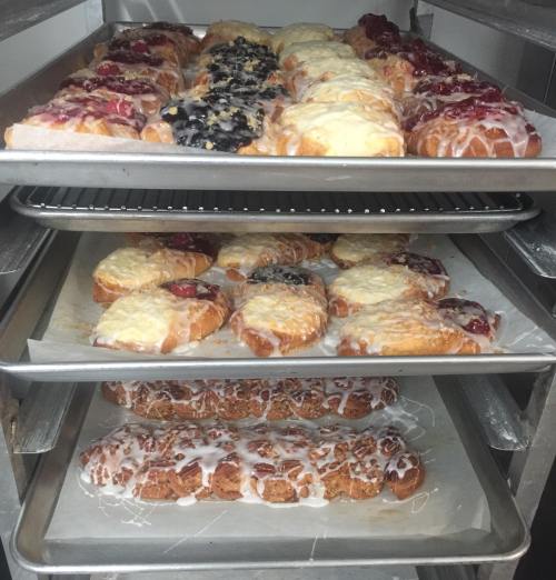 A display of freshly baked pastries on trays, featuring various fruit toppings and icing.