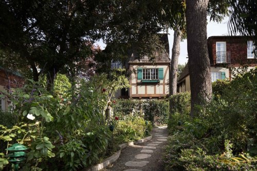 A charming garden path leads to a quaint house surrounded by lush greenery and trees.