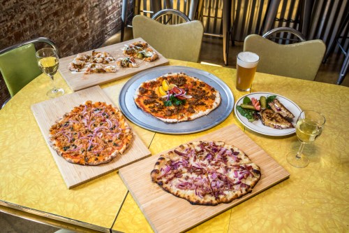 A vibrant table setting featuring various pizzas, appetizers, and drinks on a yellow tablecloth.