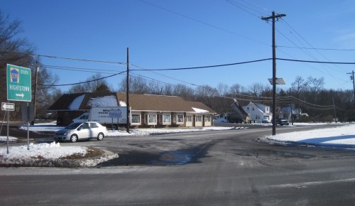 A snowy intersection with a sign for Wightstown, featuring a building and a car on a clear day.