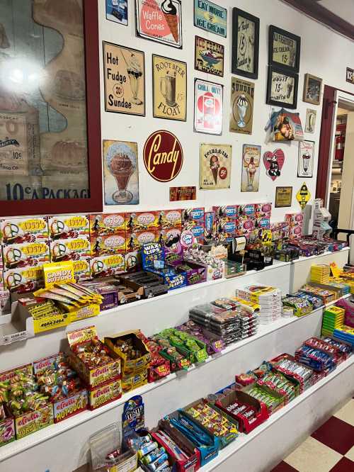 A colorful display of various candies and snacks on shelves, with vintage signs and posters on the wall behind.