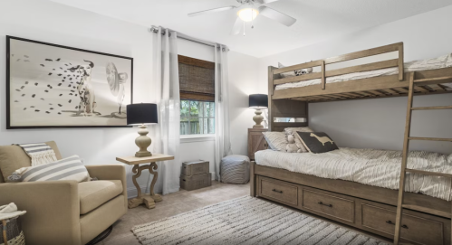 Cozy bedroom with a bunk bed, armchair, and decorative artwork, featuring soft lighting and neutral tones.