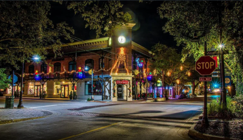 A charming street scene at night, featuring a clock tower, festive lights, and a stop sign amidst trees.
