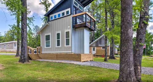 A modern two-story house with a wooden deck, surrounded by trees and other homes in a serene outdoor setting.