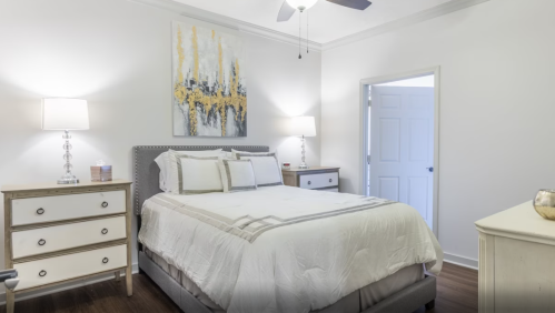 A bright, modern bedroom featuring a queen bed, nightstands, lamps, and a colorful wall art piece.