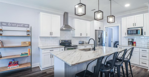 Modern kitchen with white cabinets, marble island, stainless steel appliances, and a bookshelf filled with books.