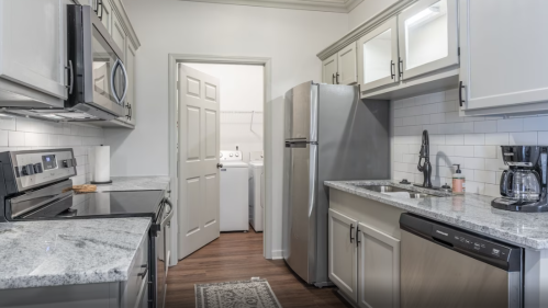 Modern kitchen with stainless steel appliances, granite countertops, and a laundry area visible through an open door.