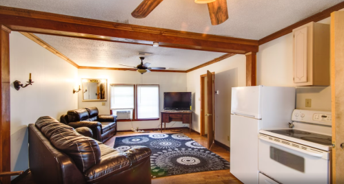 Cozy living room with leather sofas, a TV, and a kitchen area featuring a stove and refrigerator.