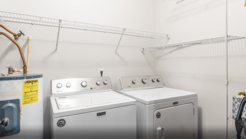 A laundry room featuring a washer and dryer with a shelf above, and a water heater on the left.
