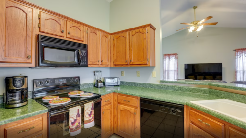 A cozy kitchen with wooden cabinets, green countertops, and modern appliances, including a stove and coffee maker.