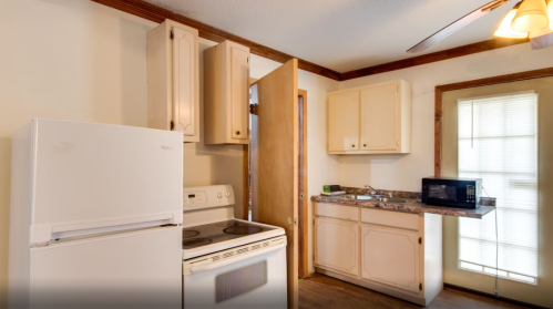 A small kitchen featuring a white refrigerator, stove, microwave, and light-colored cabinets with a door leading outside.
