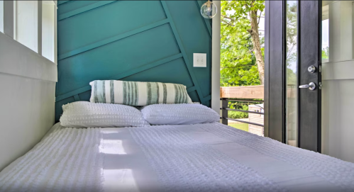 Cozy bedroom with a bed, striped pillows, and large windows overlooking greenery.