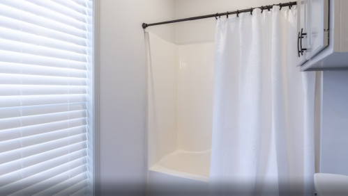 A clean bathroom with a white shower curtain and a window with blinds, featuring a bathtub and light-colored walls.