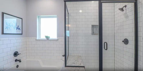 Modern bathroom featuring a glass shower, white subway tiles, a bathtub, and a window with natural light.