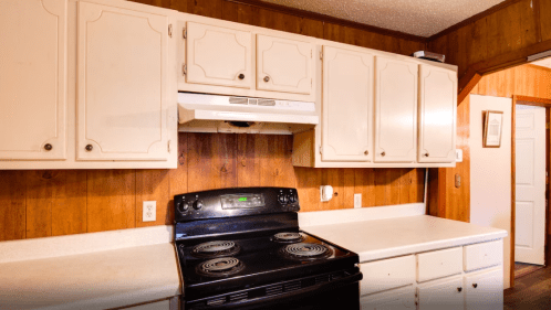 A kitchen with wooden walls, white cabinets, and a black stove with an overhead range hood.