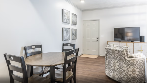 A cozy living space featuring a round dining table, chairs, a TV, and decorative wall art.