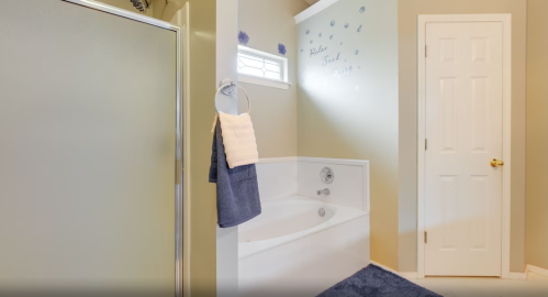 Bright bathroom featuring a shower, a white bathtub, and decorative wall accents in soft colors.