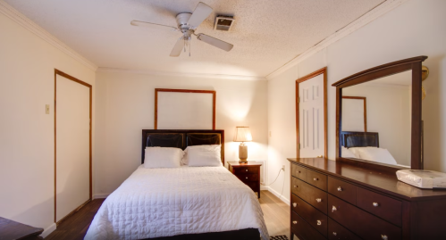 Cozy bedroom featuring a bed, dresser, mirror, lamp, and ceiling fan in a softly lit space.