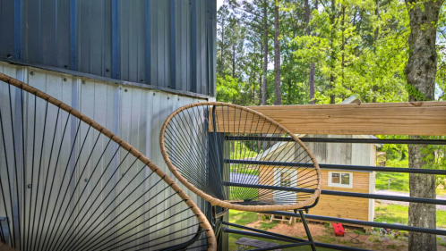 A cozy balcony view featuring a stylish chair and a glimpse of greenery and a small cabin in the background.