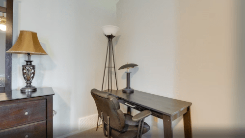 A minimalist workspace featuring a desk, chair, and two lamps in a softly lit room.