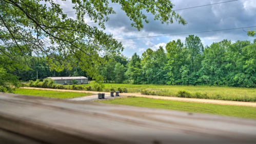 A rural landscape featuring a grassy field, trees, and a distant building under a cloudy sky.