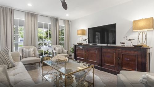 Bright living room with a TV, elegant furniture, and large windows, featuring neutral tones and decorative accents.