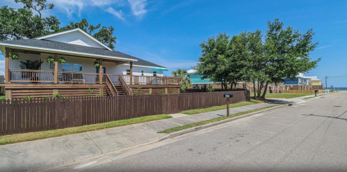 A quiet street lined with houses and greenery, featuring wooden fences and a clear blue sky.