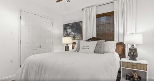 Cozy bedroom with a white bed, decorative pillows, two lamps, and a large window with curtains.
