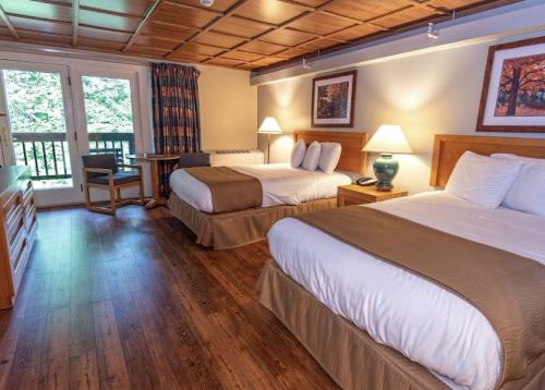 Cozy hotel room with two beds, wooden floors, and a balcony view, featuring warm lighting and nature-themed decor.