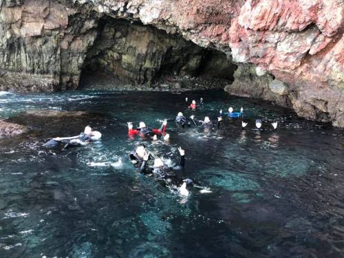 A group of people swimming in a rocky cove, surrounded by clear water and cliffs.