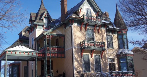 A large, ornate Victorian house with multiple gables, balconies, and colorful trim against a clear blue sky.
