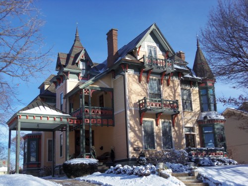 Victorian-style house with ornate details, multiple gables, and snow-covered yard under a clear blue sky.