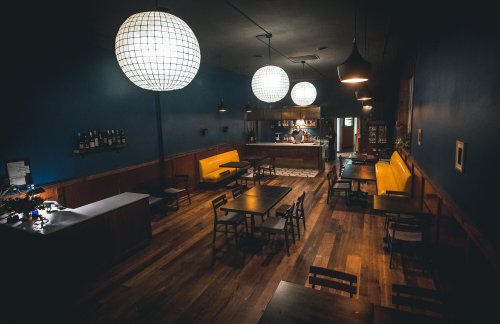 A cozy restaurant interior with wooden floors, yellow seating, and large pendant lights illuminating the space.