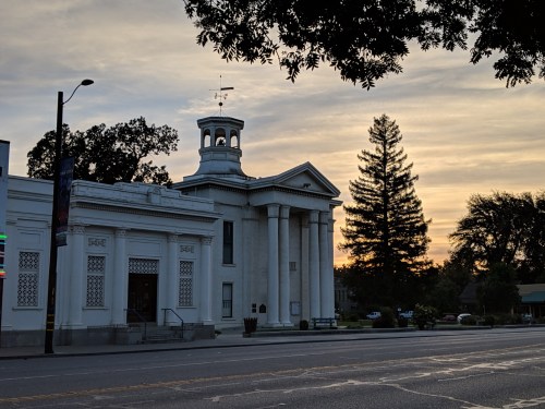 Historic white building with columns at sunset, surrounded by trees and a quiet street.