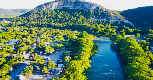 Aerial view of a lush green landscape with a river, trees, and a mountain in the background.