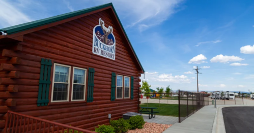 Log cabin-style building of Buckhorn RV Resort with green shutters, picnic area, and blue sky in the background.