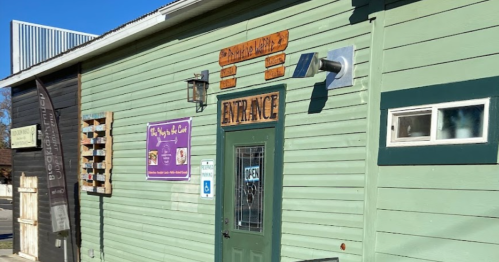 A green building with a wooden "Entrance" sign and an "Open" sign, featuring a purple banner on the wall.