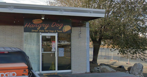 Exterior of "Hangry Dog" restaurant featuring a sign for street-style hot dogs and tacos, with a parked vehicle nearby.
