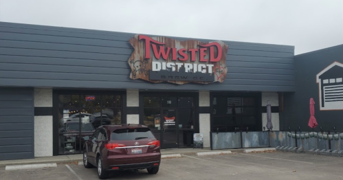 Exterior of Twisted District Brew Co. with a sign, a parked car, and bike racks in front. Overcast sky.