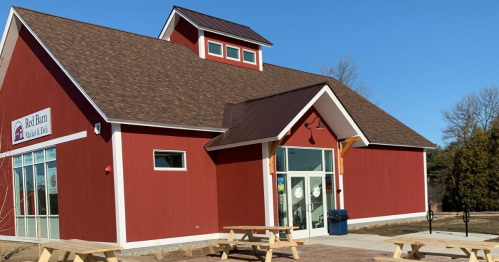 A red barn-style building with a peaked roof and large windows, surrounded by picnic tables on a sunny day.